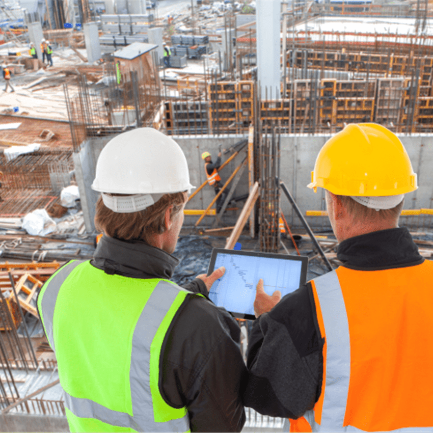 Zwei Bauarbeiter mit Schutzhelmen und Warnwesten betrachten ein Tablet auf einer Baustelle. Zwei Bauarbeiter mit Schutzhelmen und Warnwesten betrachten ein Tablet auf einer Baustelle.