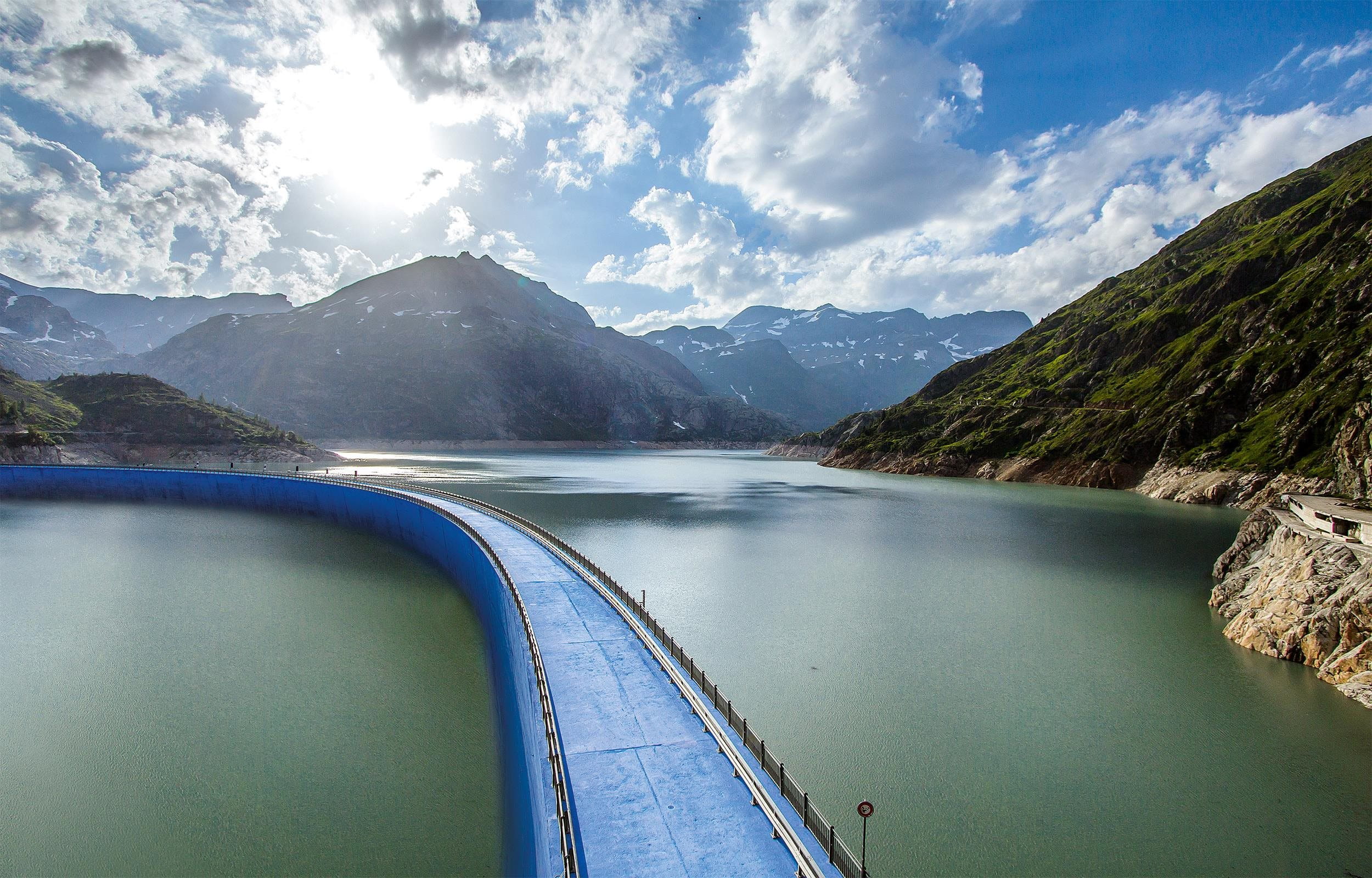 A blue bridge over a lake between a mountain landscape