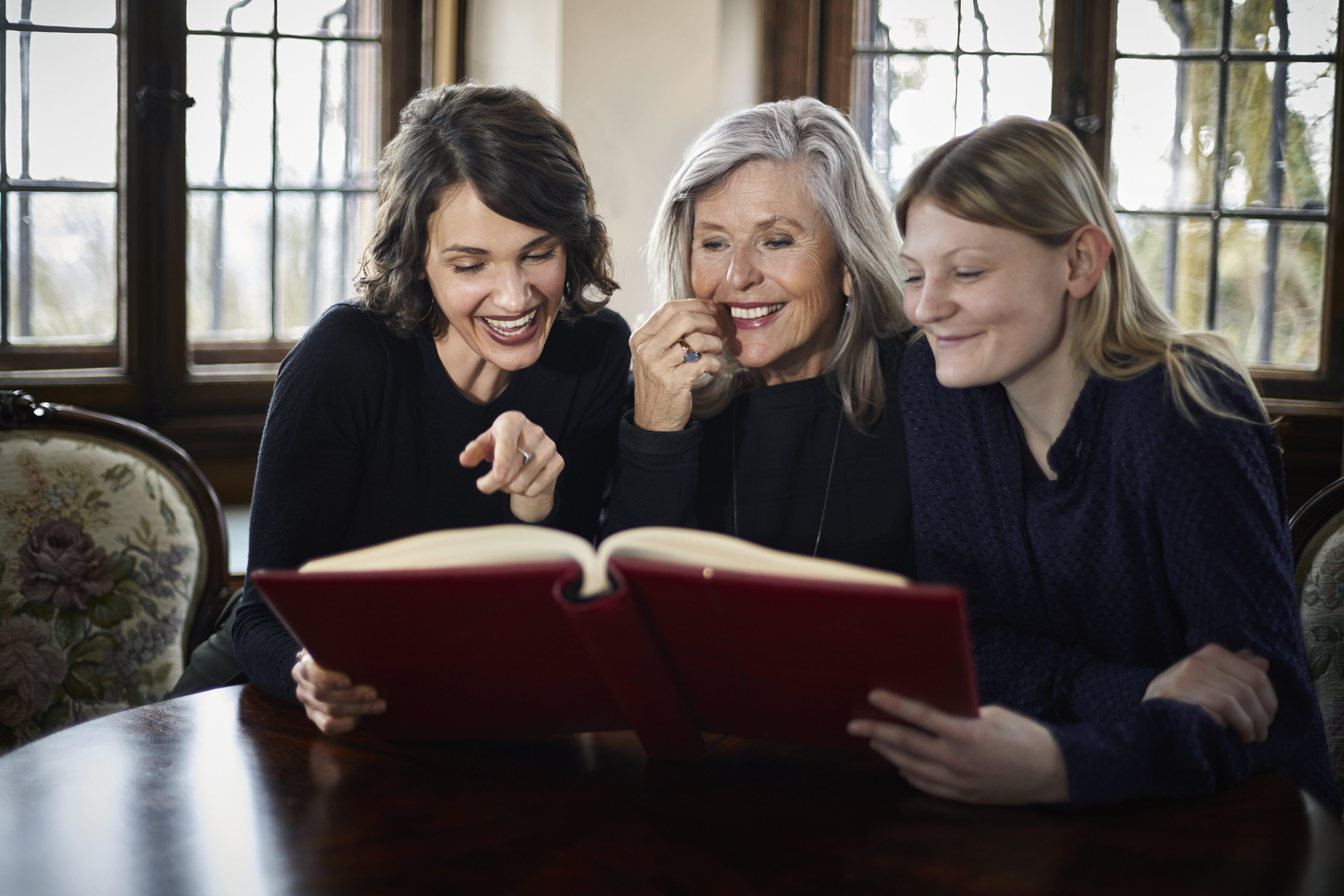 Drei Generationen von Frauen sitzen an einem Tisch und schauen ein Buch an